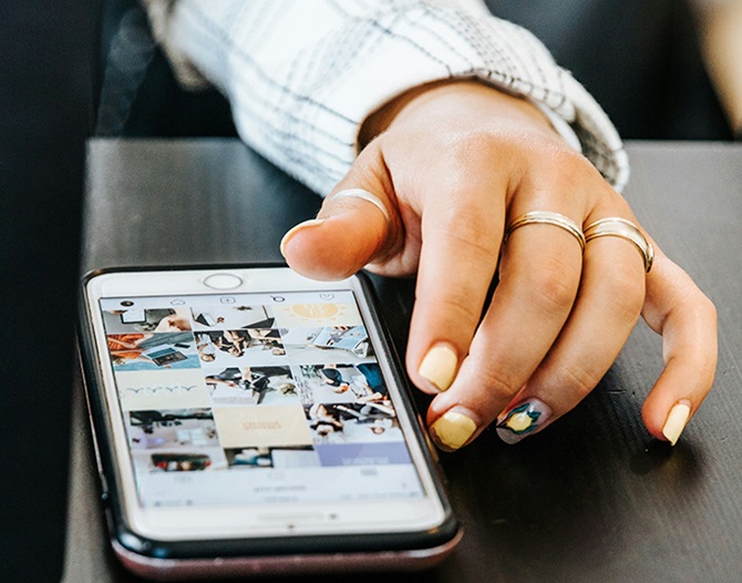 En ung kvinna scrollar bland bilder i mobilen.