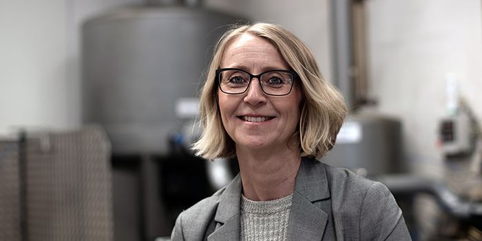 En kvinna i grå kavaj som ler mot kameran i en industrilokal