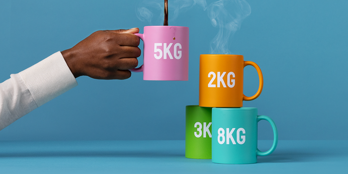 En hand som håller upp en kopp märkt med 5 kg, brevid står tre koppar märkta med tre, fem och åtta kilo.