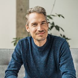 Man i blå stickad tröja som tittar in i kameran.