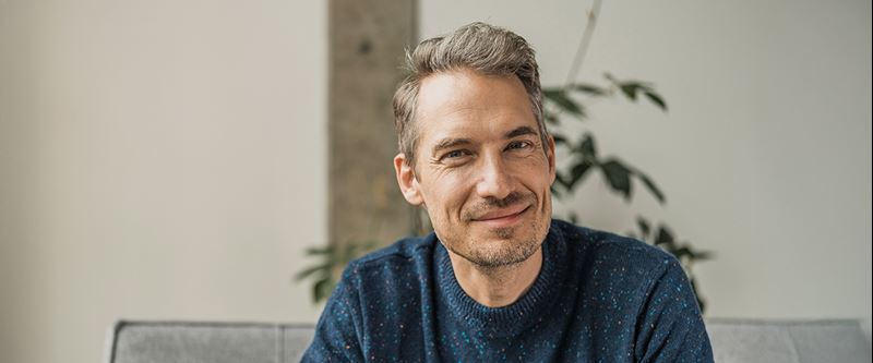 Man i blå stickad tröja som tittar in i kameran.