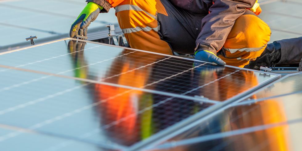 Person i orangea skyddskläder som installerar en solpanel.