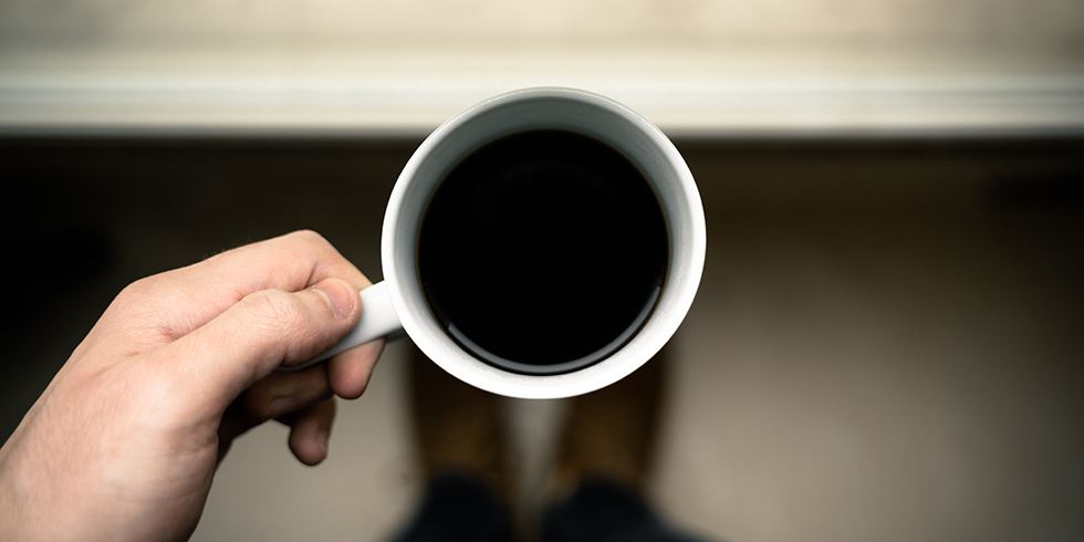 Hand som håller i en vit kaffekopp.