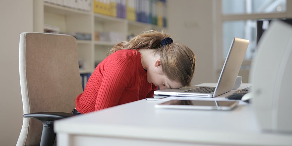 En kvinna lutar huvudet mot tangentbordet på sin laptop.