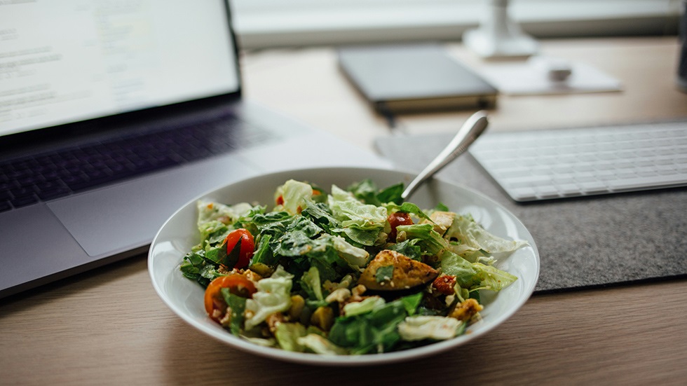En tallrik med sallad står på ett bord framför en datorskärm.
