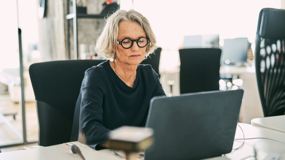 En kvinna i 60-årsåldern sitter och jobbar vid en dator.