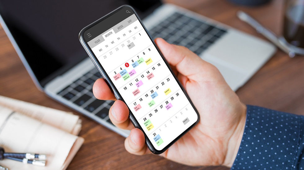 En hand som håller i en mobiltelefon med en kalenderapp.