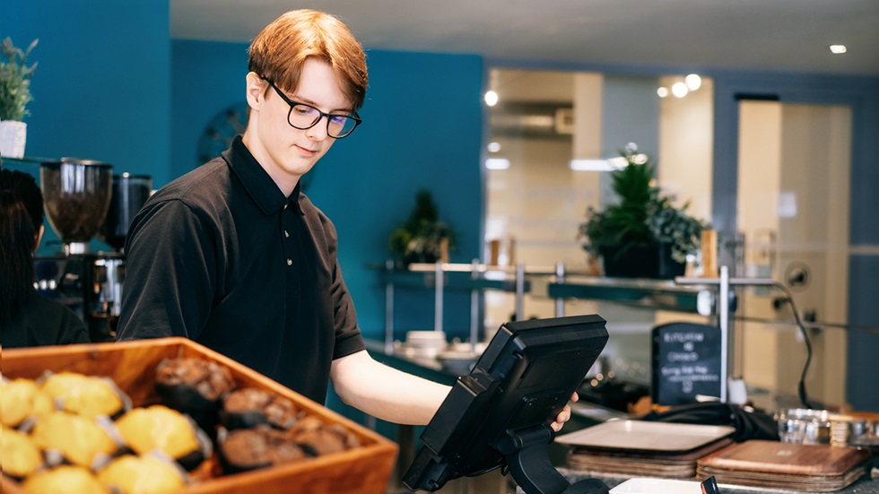 En ung kille jobbar i kassan på ett kafé.
