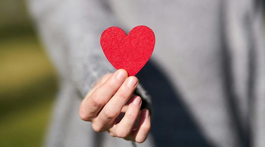Närbild på en hand som håller i ett rött pappershjärta.