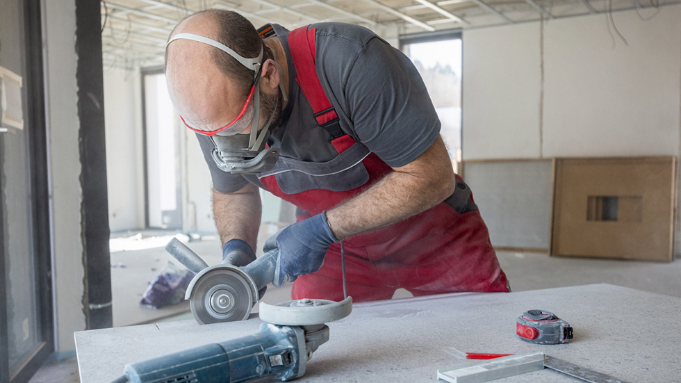 En byggnadsarbetare med andningsskydd skär i en bänskiva.