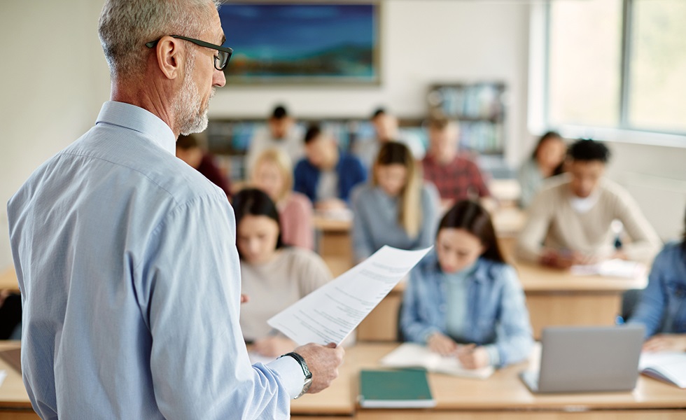 En äldre lärare undervisar elever i klassrum.