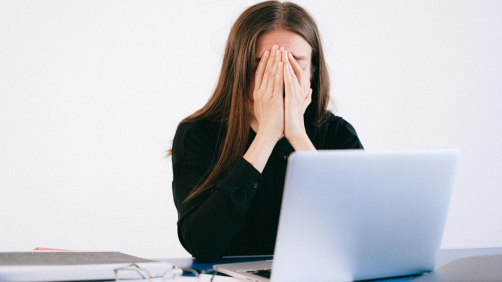 En kvinna sitter med ansiktet i händerna vid sitt skrivbord på jobbet.