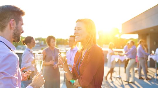 En personalfest där man ser kollegor prata med ett glas vin i handen.