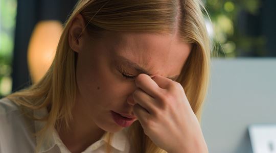 Ljushårig kvinna i kontorsmiljö håller sig för ansiktet och ser fundersam ut.