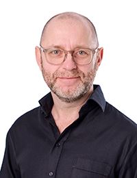 Man i glasögon och mörk skjorta som ler.