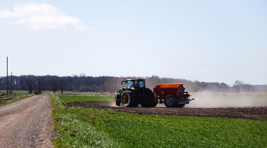Grön och röd traktor som kör över ett soligt, grönt fält.