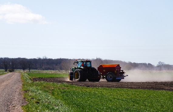 Grön och röd traktor som kör över ett soligt, grönt fält.