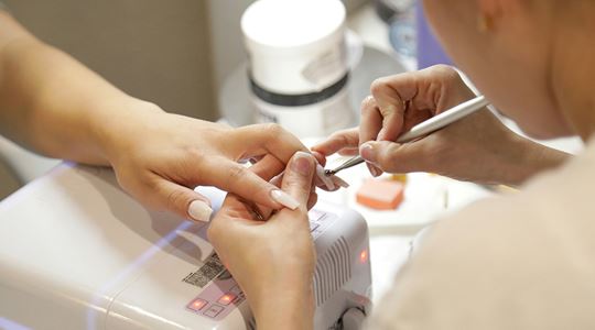En kvinna får sina naglar målade av en nagelterapeut.