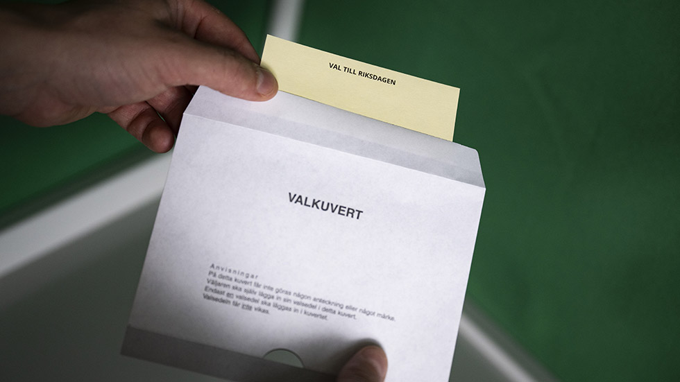 En person lägger en valsedel i ett valkuvert.
