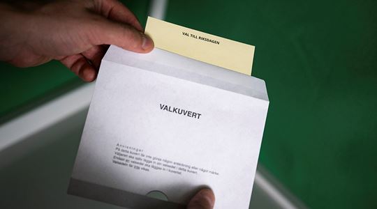 En person lägger en valsedel i ett valkuvert.