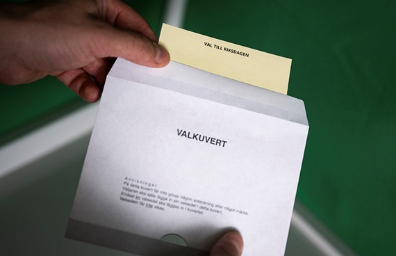 En person lägger en valsedel i ett valkuvert.