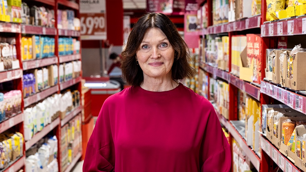 Mörkhårig kvinna i mataffär som tittar rakt in i kameran.