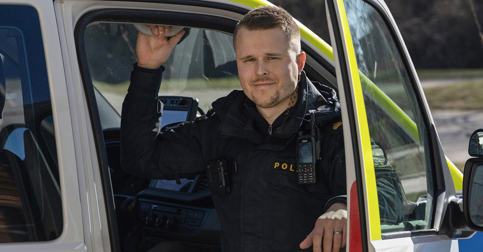 Christoffer Nydal, i polisuniform sitter i en polisbil med öppen dörr.