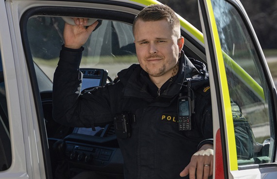 Christoffer Nydal, i polisuniform sitter i en polisbil med öppen dörr.