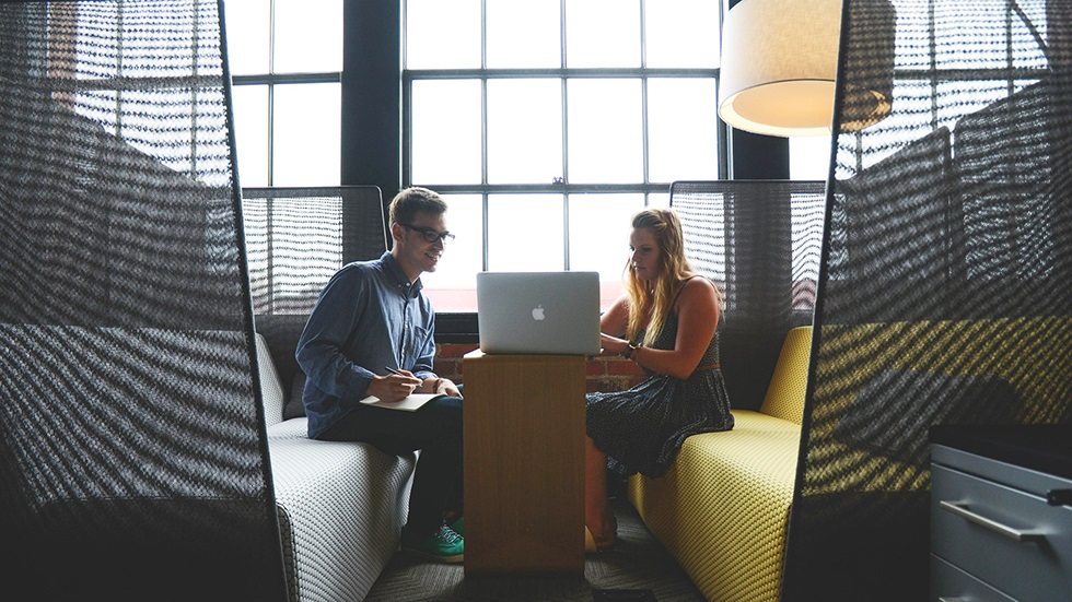 Två kollegor sitter mittemot varandra och tittar på en skärm som står på ett litet bord mellan dem. 