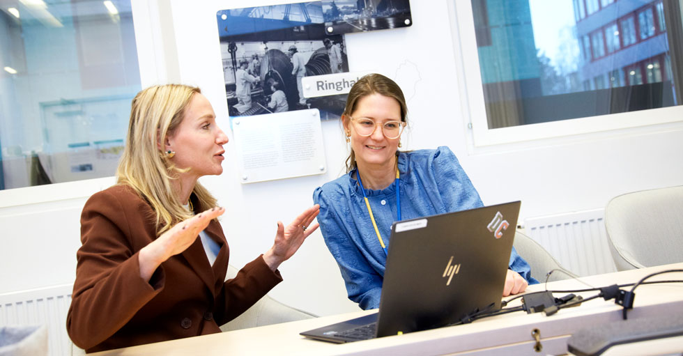 Petronella Schröder (t.h.) och hennes kollega Desirée Comstedt sitter framför en laptop vid ett skrivbord och diskuterar.