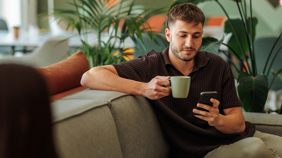 En man sitter och tittar på sin mobil under en fikapaus på jobbet.
