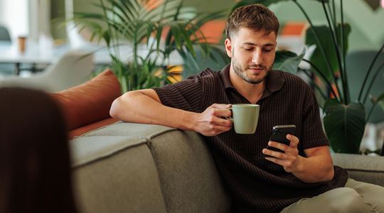 En man sitter och tittar på sin mobil under en fikapaus på jobbet.