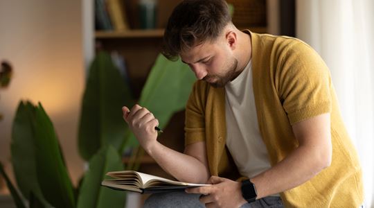 En man sitter böjd över en anteckningsbok med en penna i handen.
