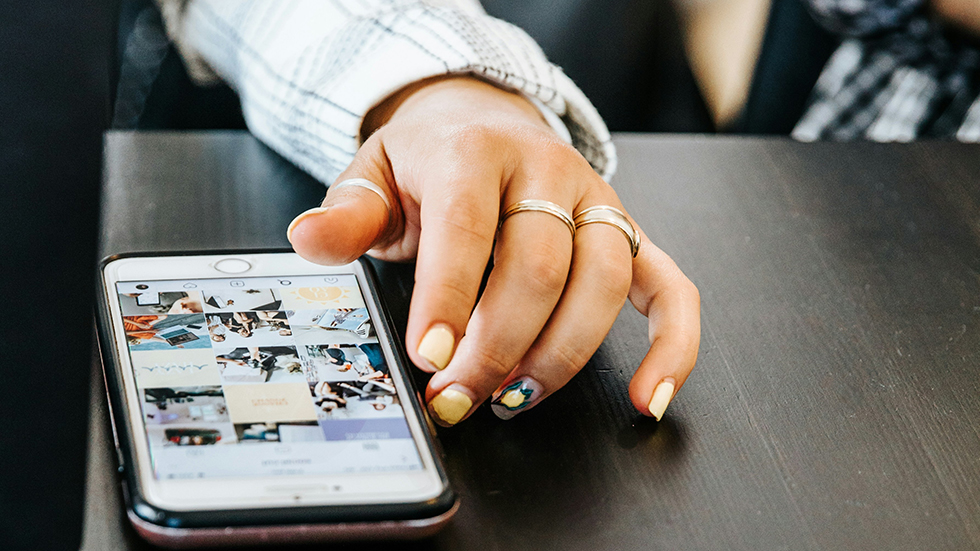 En ung kvinna scrollar bland bilder i mobilen.