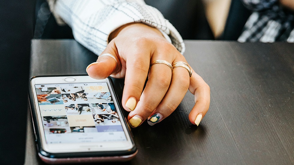 En ung kvinna scrollar bland bilder i mobilen.