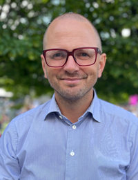 Man med glasögon och blå skjorta som tittar in i kameran.