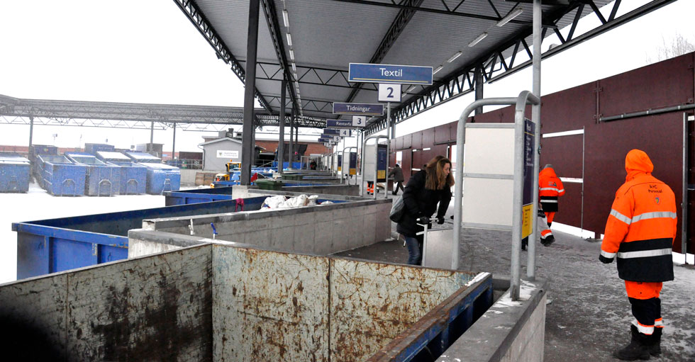 Återvinningsstation med olika containrar och personal i varselkläder.
