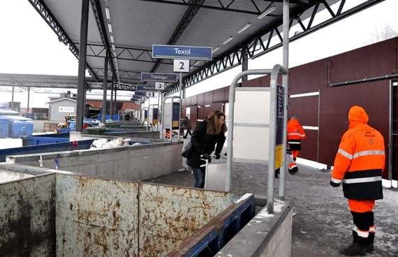 Återvinningsstation med olika containrar och personal i varselkläder.