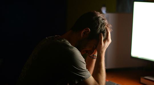 En man sitter med huvudet i händerna framför en dataskärm