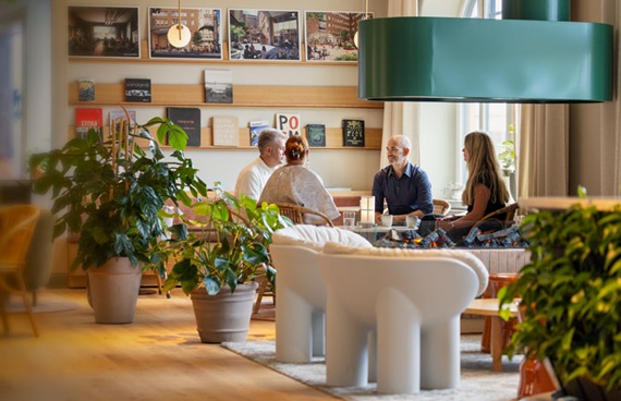 En grupp människor sitter och samtalar i ett hörn av ett kontor. Inredningen är varm med mycket trä och växter.
