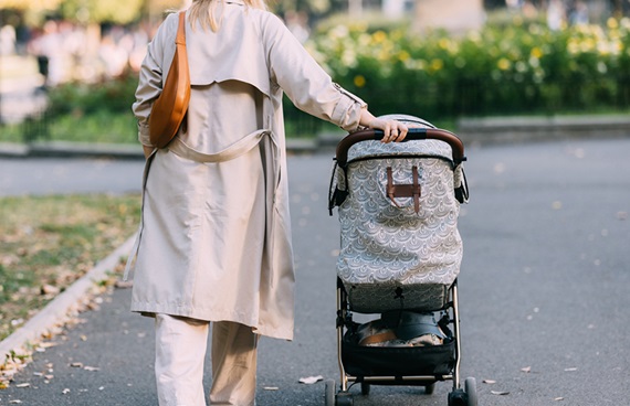 En kvinna promenerar i en park med en barnvagn.