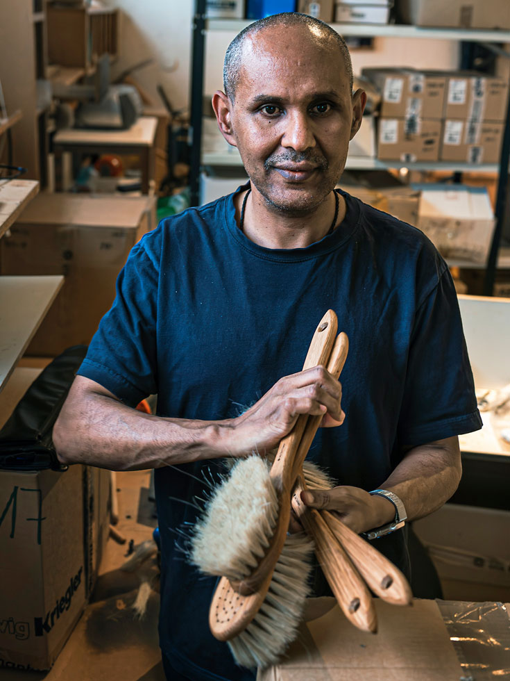 Stor porträttbild på Kubrom Ghebregiorgis, borstbindare, som håller fram en bunt badborstar i handen.